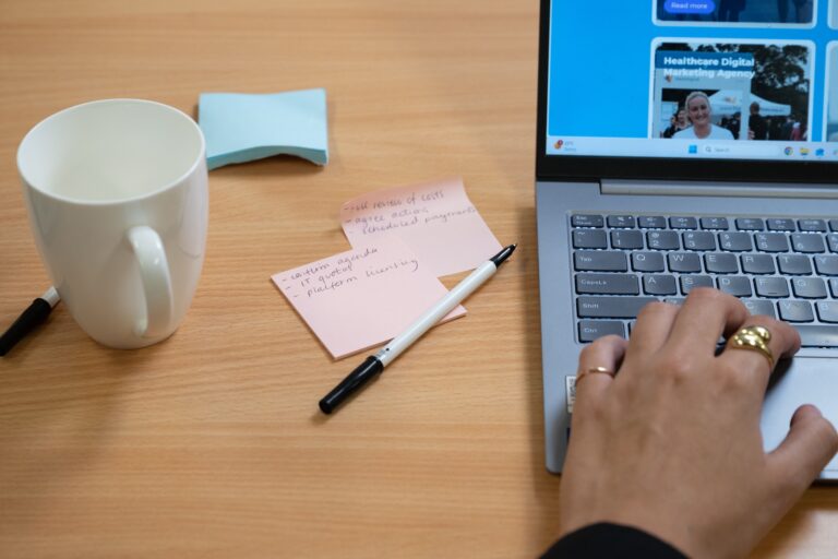 A desk with a laptop, handwritten notes and a coffee cup